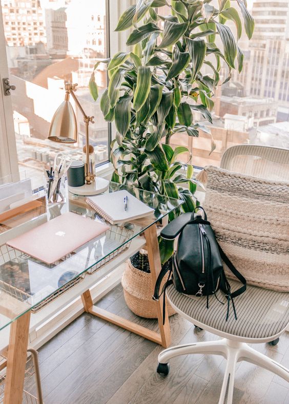 ένας μοντέρνος χώρος εργασίας boho με ένα γραφείο από γυαλί και ξύλο, μια άνετη καρέκλα, ένα μαξιλάρι boho και ένα φυτό σε γλάστρες, τζάμια στους τοίχους για εκπληκτική θέα
