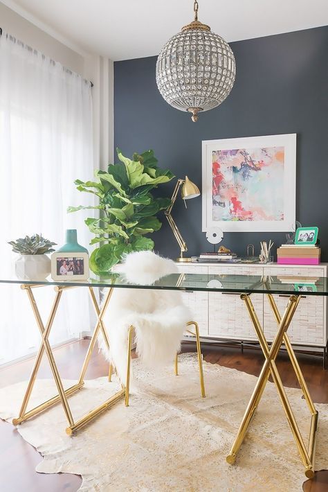 ένα glam home office με ένα γυάλινο και χρυσό γραφείο, μια χρυσή καρέκλα με γούνα, ένα κρυστάλλινο φωτιστικό και τολμηρή τέχνη